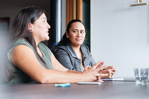 Two Maori women on one side of table in involved in discussion using te reo maori during business meeting
